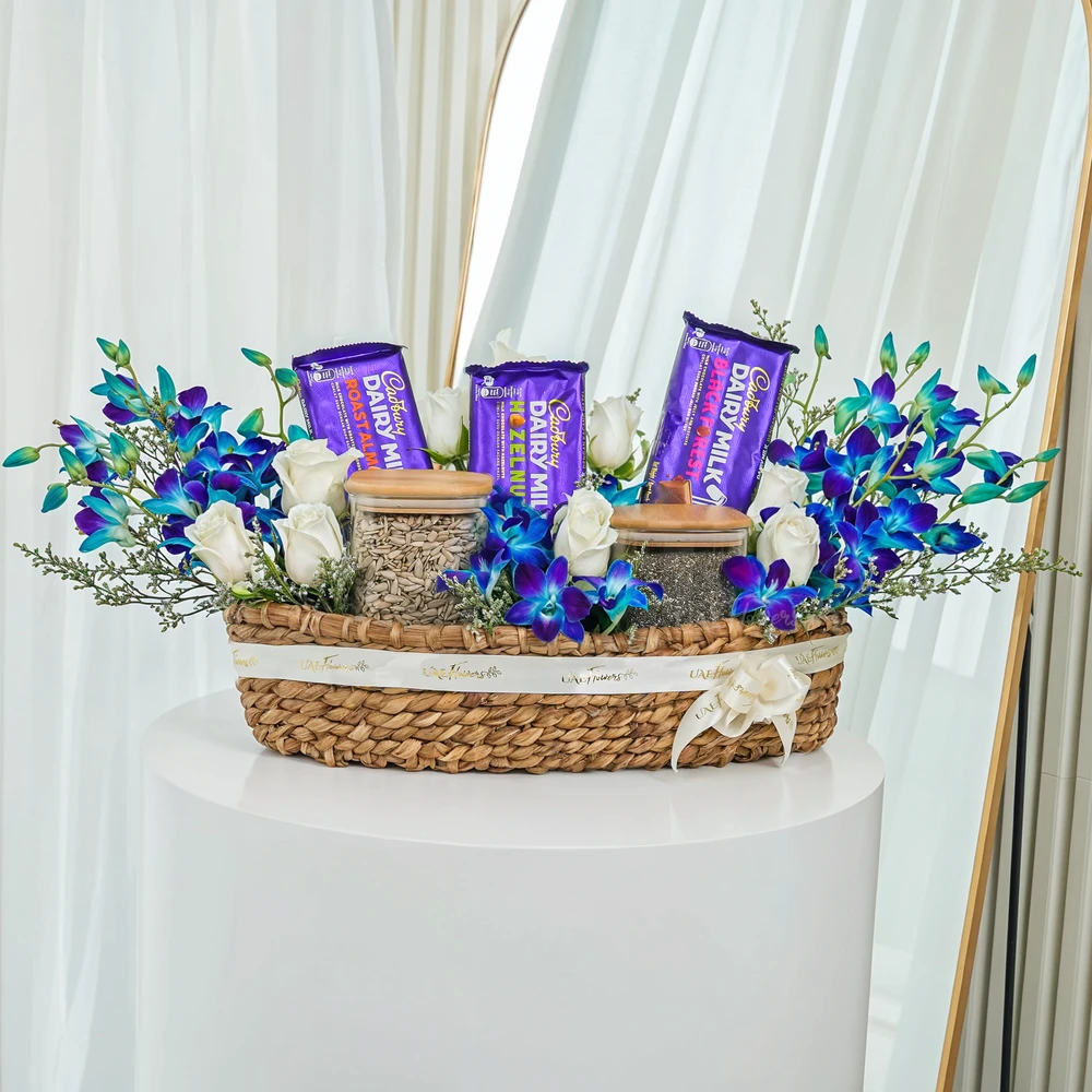 10 white roses, 5 blue orchids, 3 pcs of cadbury dairy milk chocolate, 250 Gms of Sunflower Seeds, 250 Gms of Chia Seeds with limonium fillers in a basket.