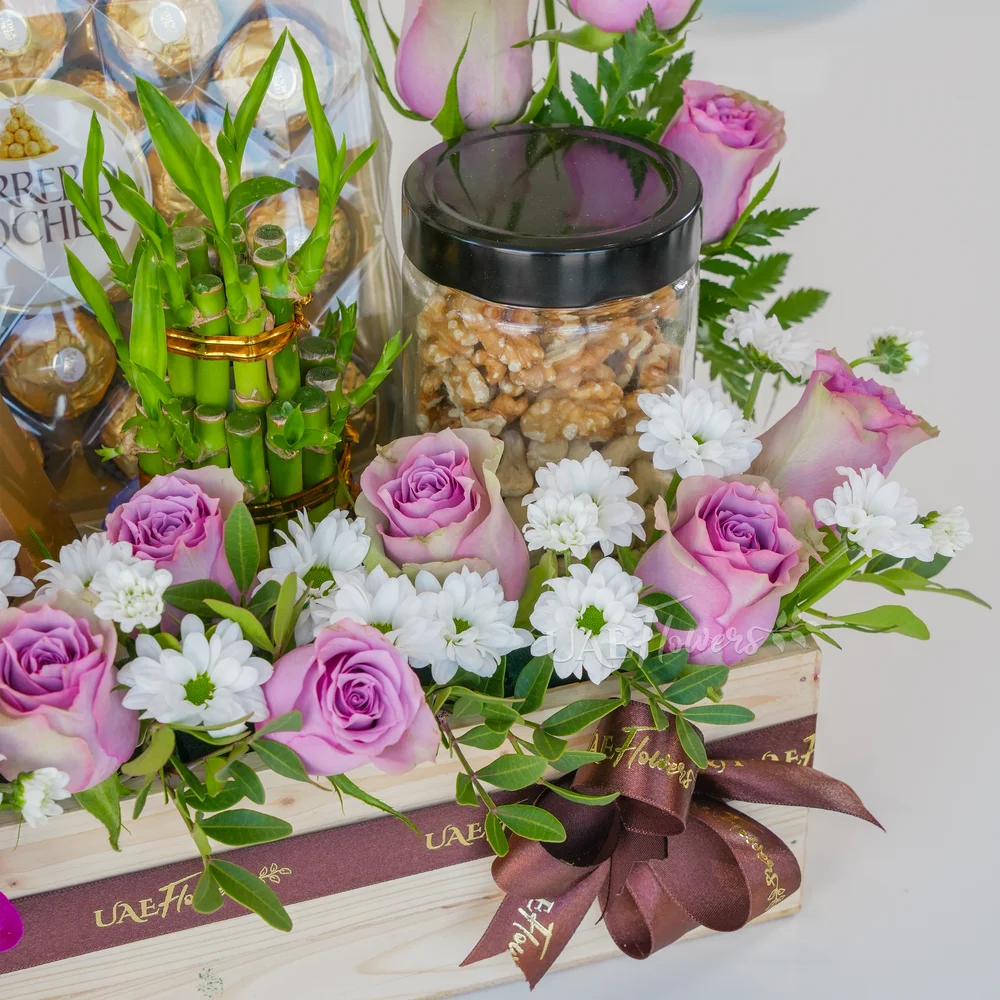 A wooden box arrangement of 10 pink roses, 5 purple orchids, white chrysanthemums, 250Gms of walnut in jar, 2 layer lucky bamboo, 24pcs of ferrero rocher chocolate and lindt lindor assorted chocolate box 200gms with green fillers.