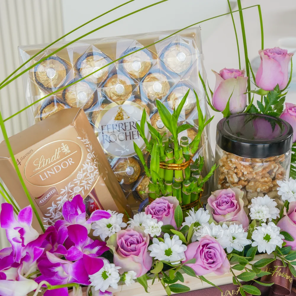 A wooden box arrangement of 10 pink roses, 5 purple orchids, white chrysanthemums, 250Gms of walnut in jar, 2 layer lucky bamboo, 24pcs of ferrero rocher chocolate and lindt lindor assorted chocolate box 200gms with green fillers.
