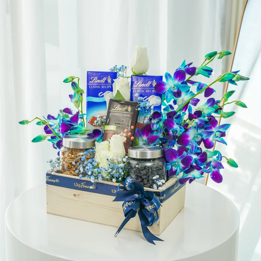 An arrangement of 5 white roses and 5 blue orchids, 250 Gms of Walnuts and 250 Gms of black raisins with 2 pcs of Lindt Swiss Classic Milk Chocolate, Lindt Swiss Classic Dark Chocolate with baby's breath fillers in a wooden box.
