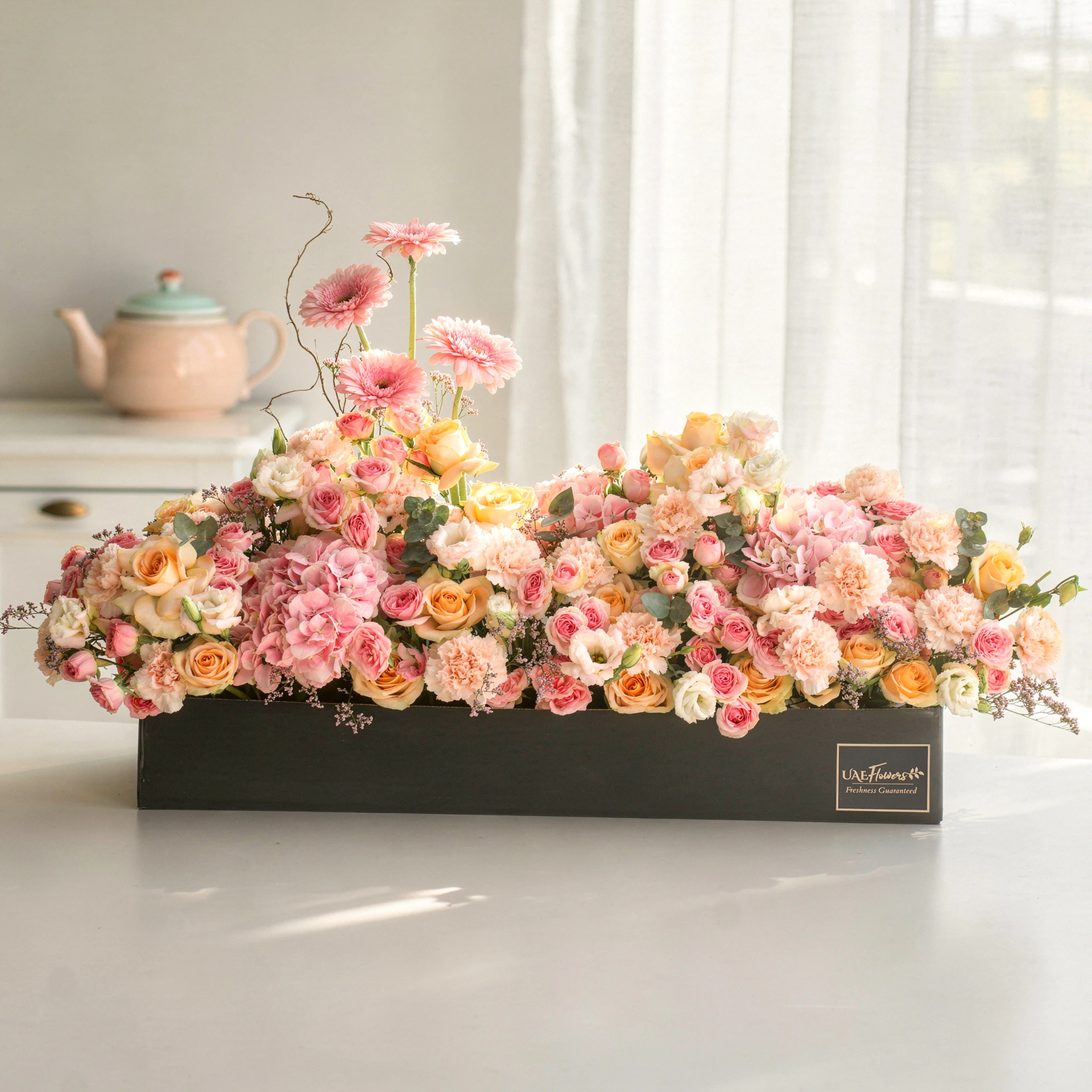 Arrangement of 4 pink gerberas, 3 pink hydrangeas, 20 pink carnations, 20 pink spray roses and 30 peach roses with green fillers in a long black box. Arrangement of 4 pink gerberas, 3 pink hydrangeas, 20 pink carnations, 20 pink spray roses and 30 peach roses with green fillers in a long black box.