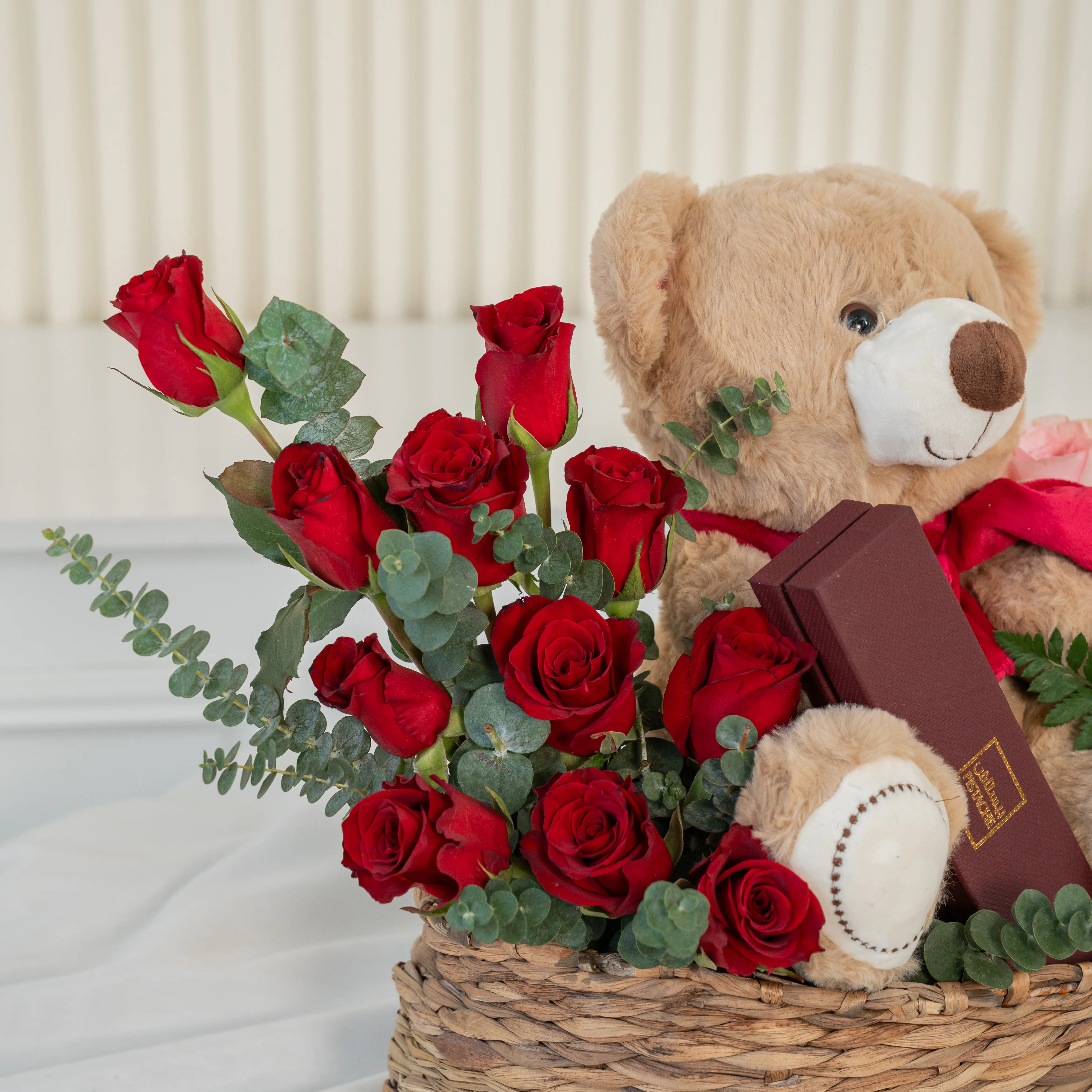 Basket arrangement of 11 red roses, 11 pink roses, small brown teddy bear and 6 Pcs Pistache Petite Indulgence Chocolate Box with green fillers.