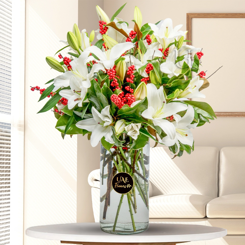 10 white lilies, magnolia, and a lot of red winterberries are gathered in a tall glass vase