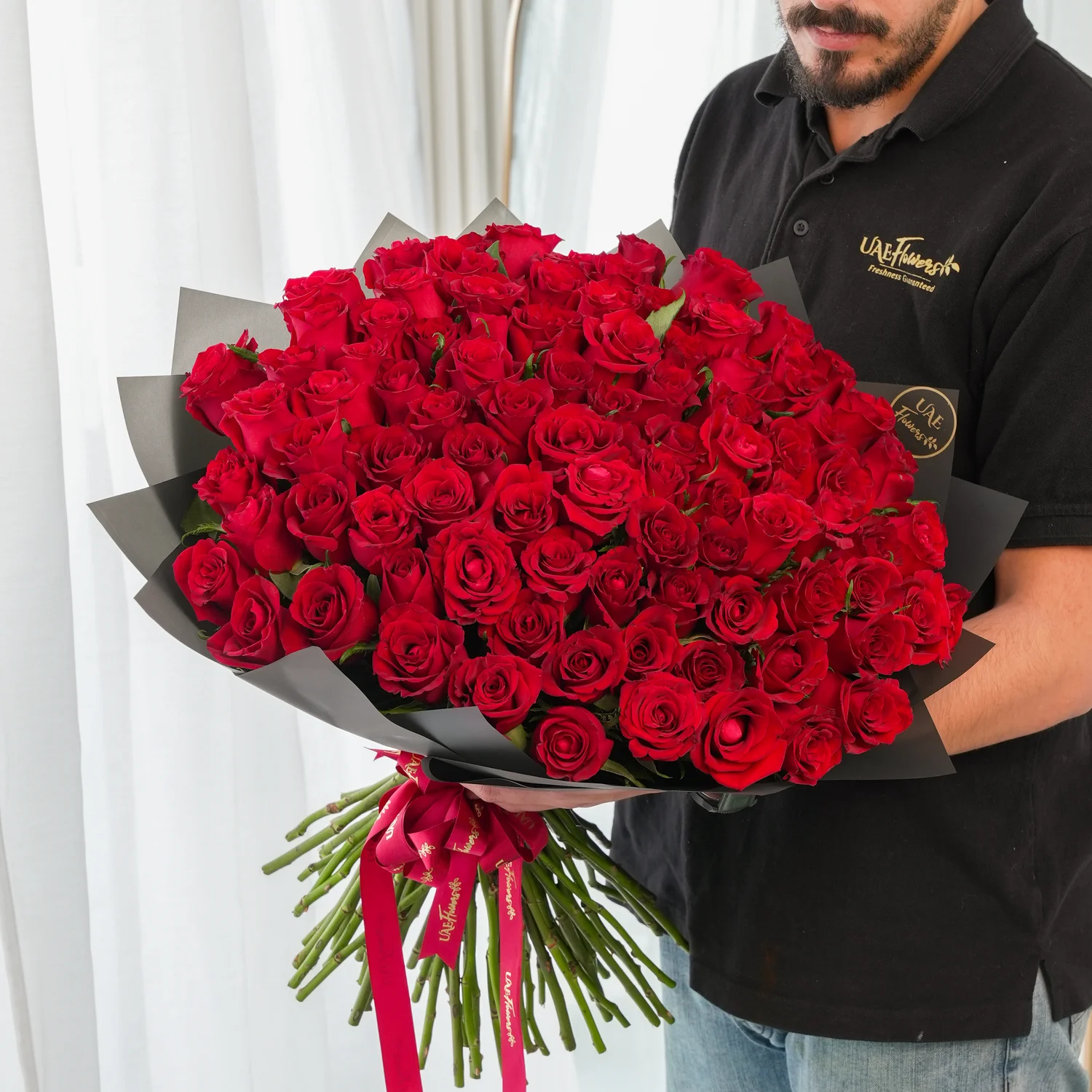 100 premium red roses hand-tied with green fillers and wrapped in black paper with satin ribbon