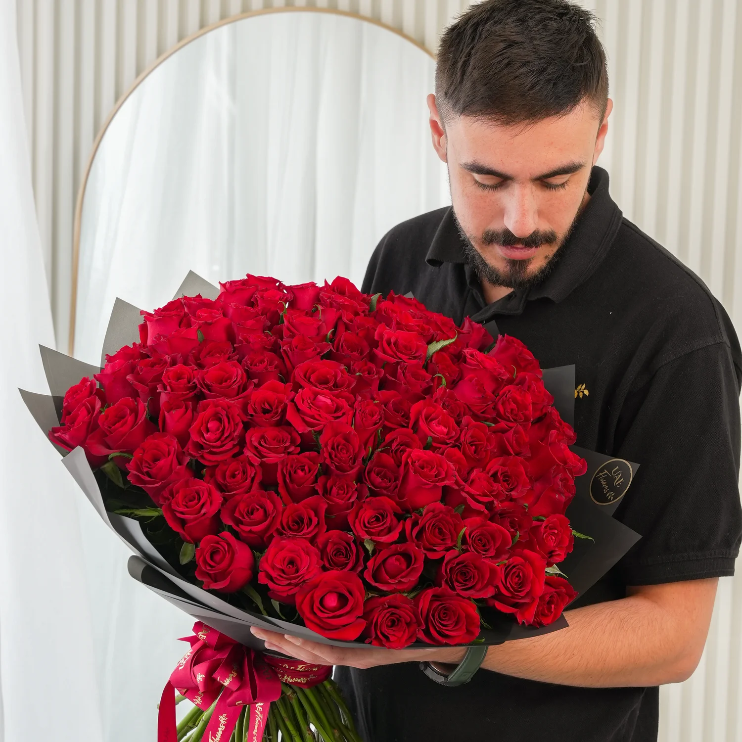 100 premium red roses hand-tied with green fillers and wrapped in black paper with satin ribbon
