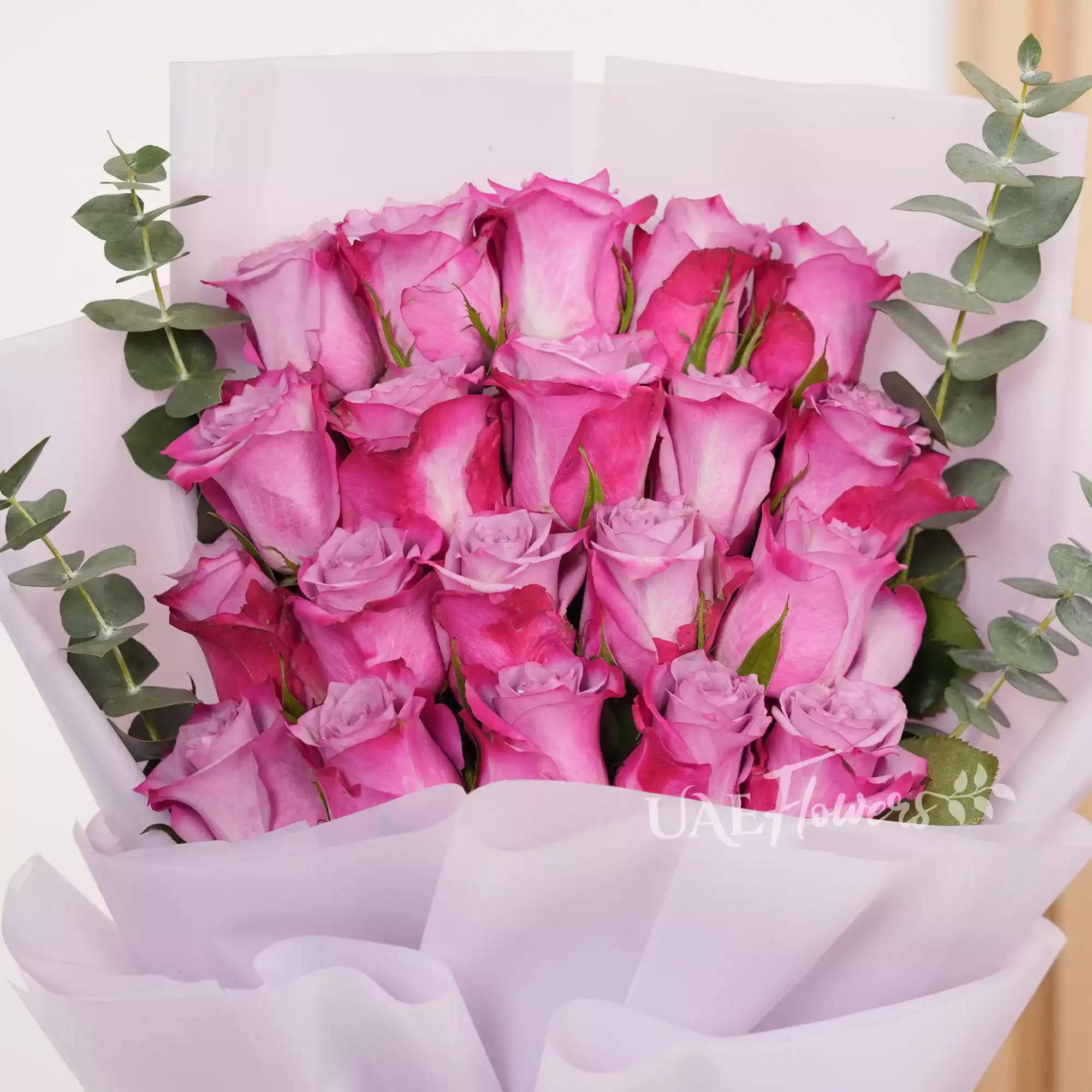 Bouquet of 20 purple roses with eucalyptus leaves, wrapped in pink paper and tied with a white satin ribbon, perfect for gifting and celebrations.