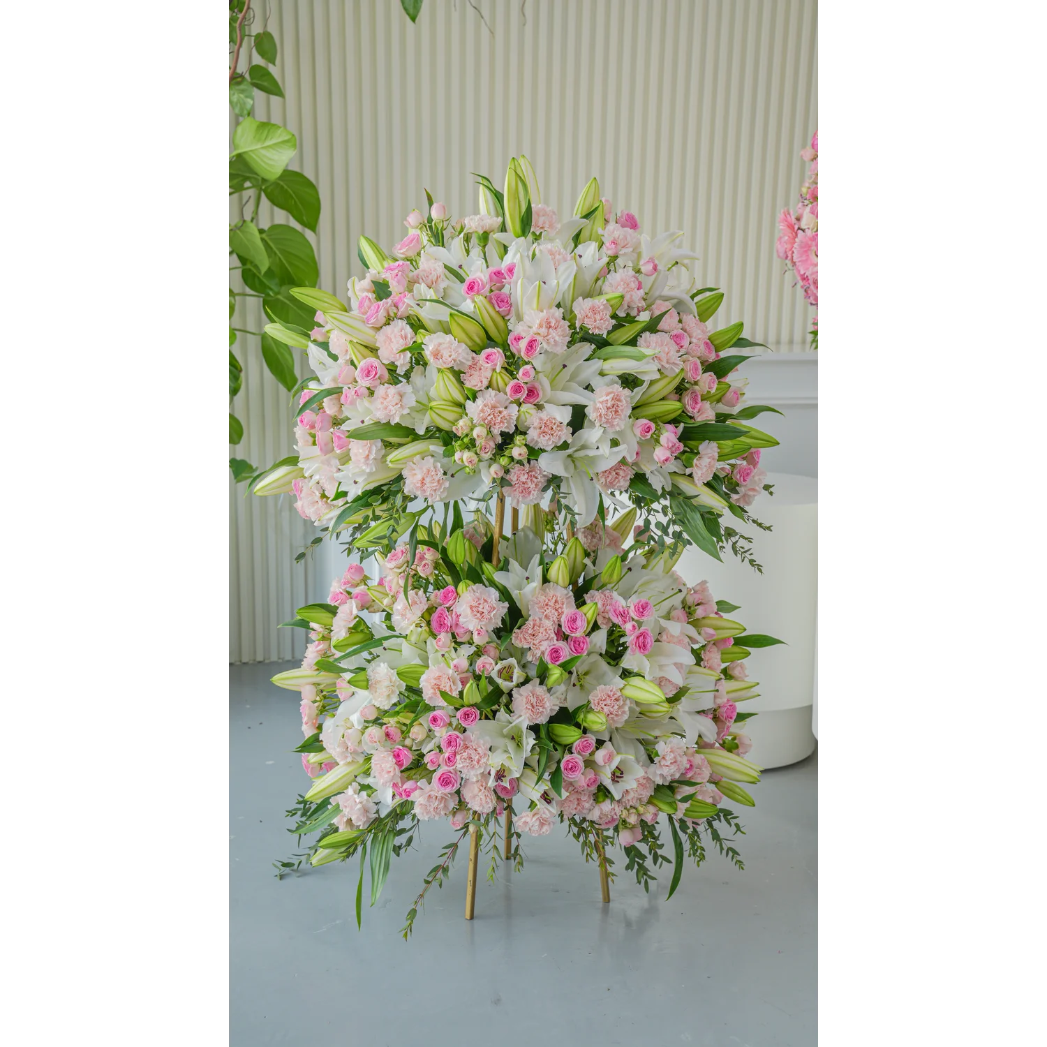 Two-tiered floral stand featuring white lilies, pink spray roses, and pink carnations with green foliage – elegant event arrangement by UAE Flowers.