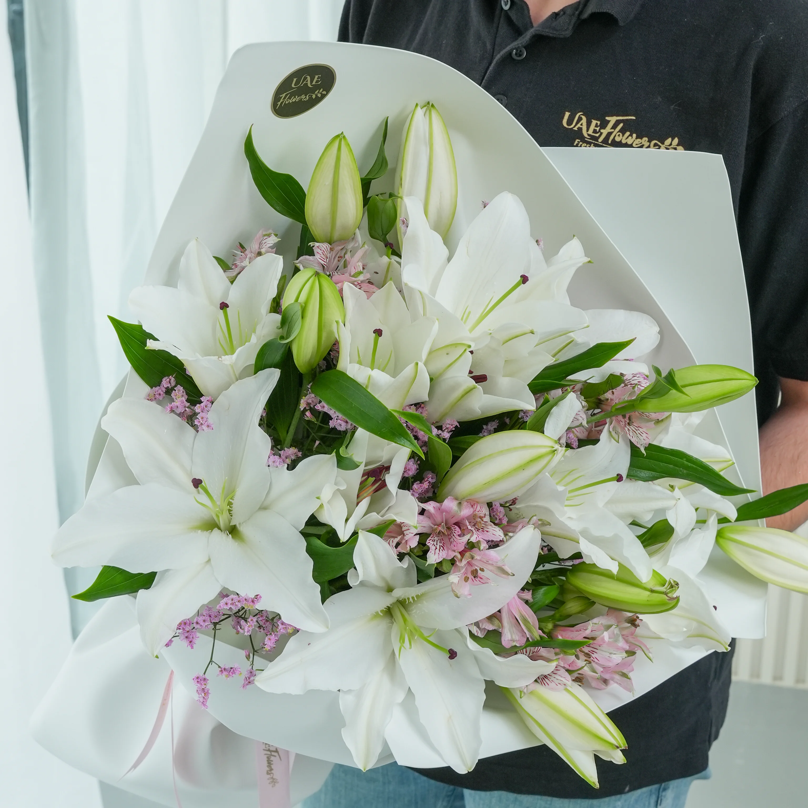 Bouquet of 5 white lilies with green fillers, wrapped in paper and tied with a ribbon.