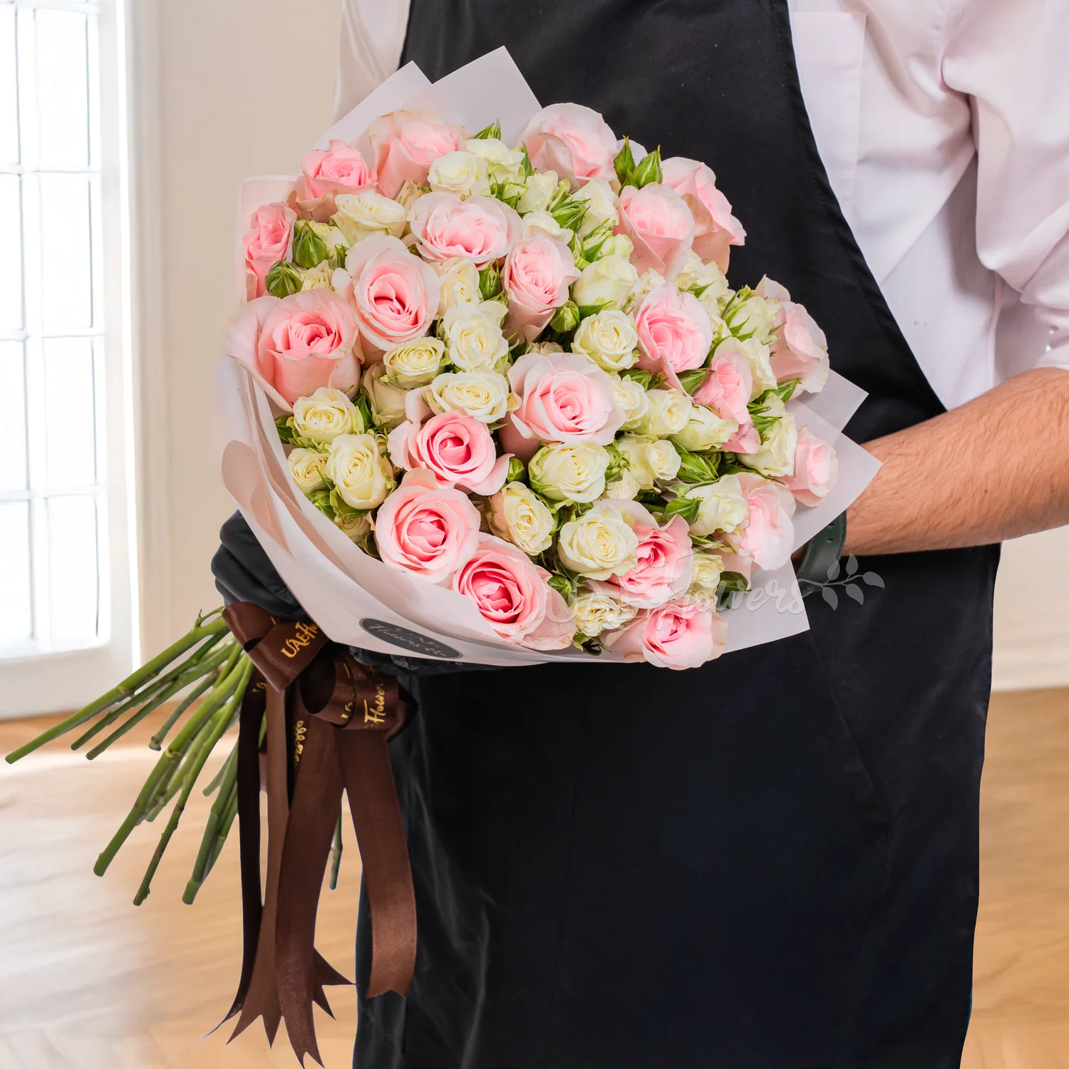 Bouquet of pink roses and white spray roses wrapped in elegant paper and tied with soft ribbons