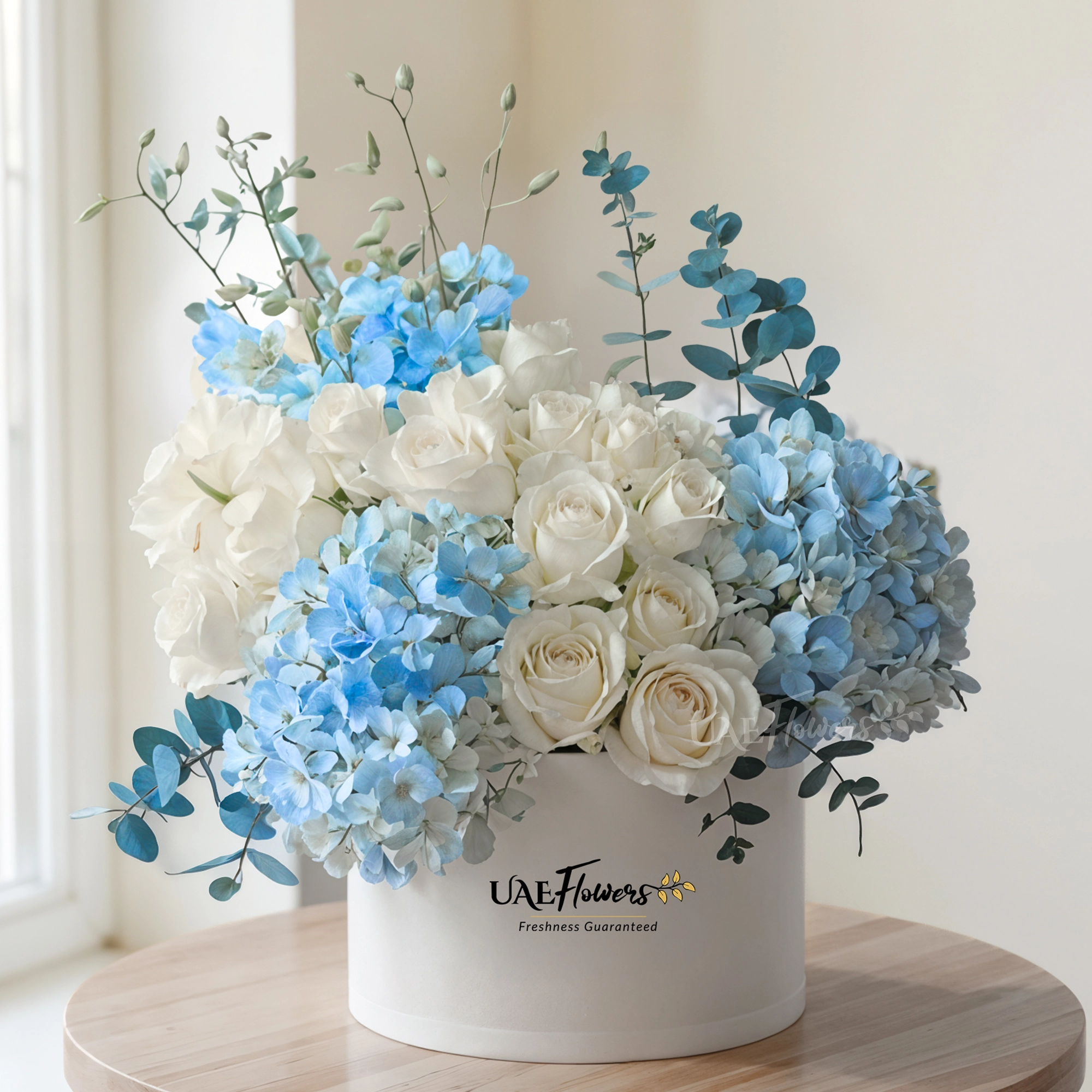 A box arrangement of 2 blue hydrangeas, 20 white roses, 5 blue orchids and blue sprayed eucalyptus leaf.
