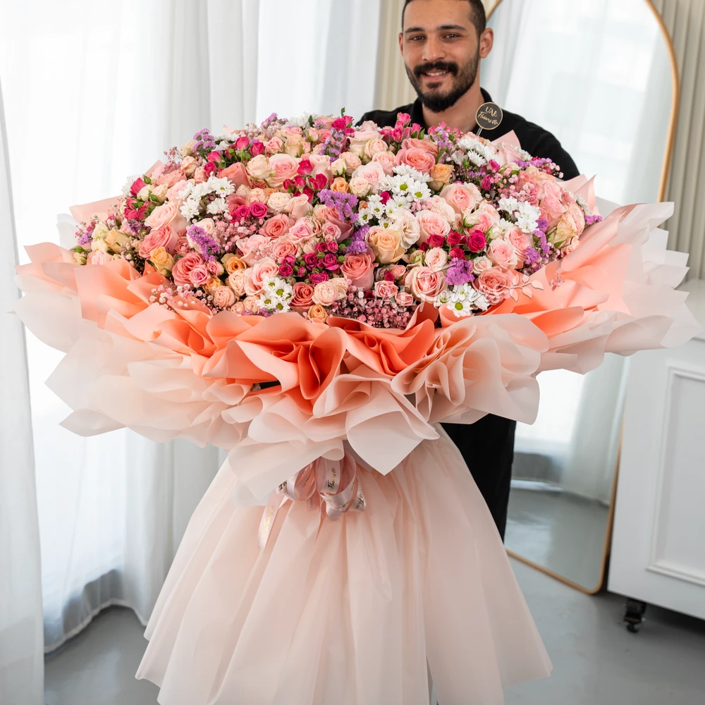 Grand bouquet of 70 mix color spray roses, 80 mix color roses and 10 white chrysanthemum with fillers in paper packing.