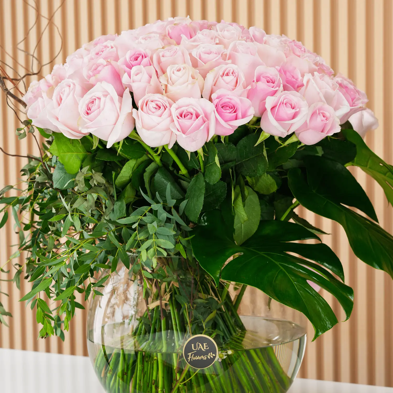 Pink Roses arrangement of 60 pink roses with lots of green fillers in a glass vase.