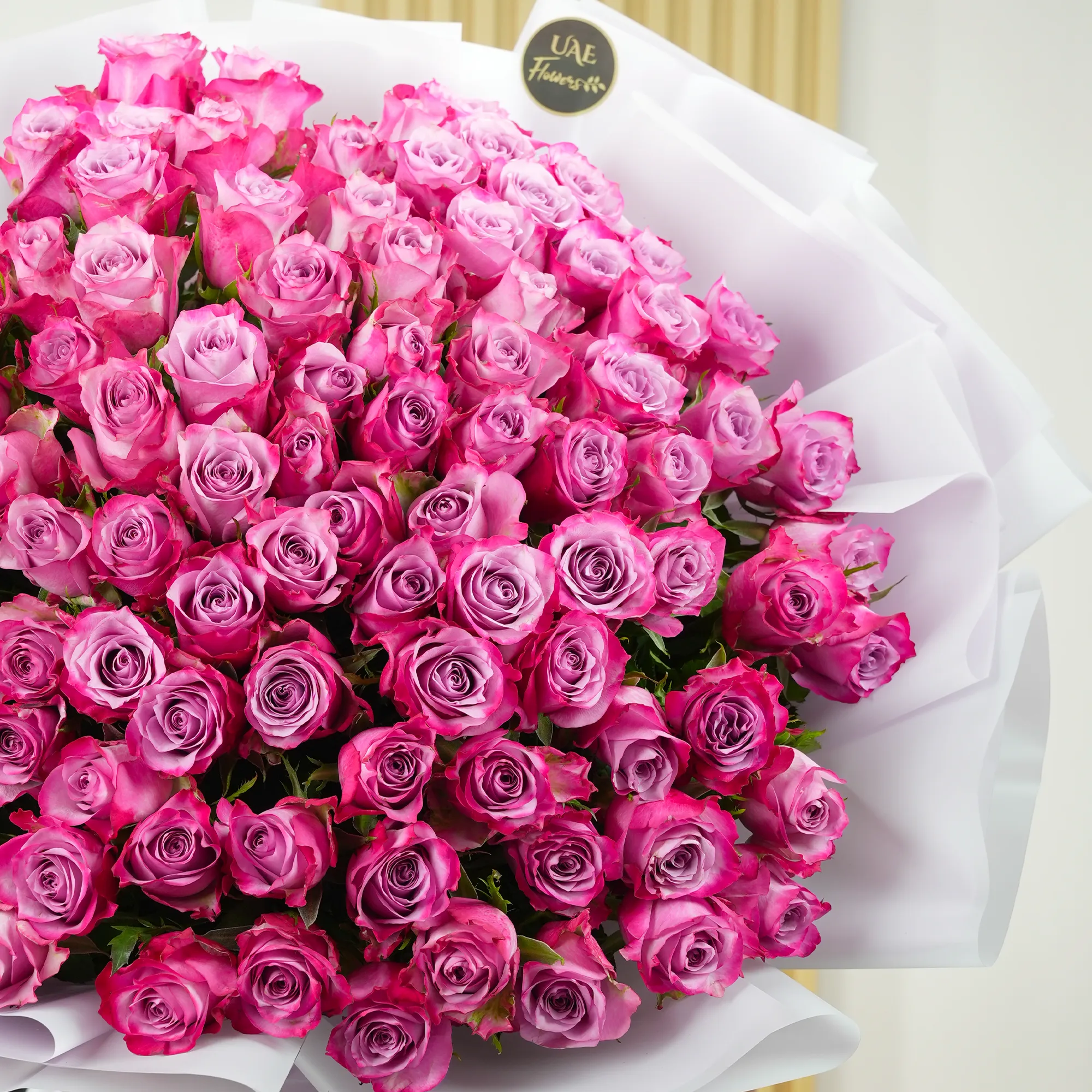 100 purple roses with fillers, wrapped in white paper and tied with ribbons