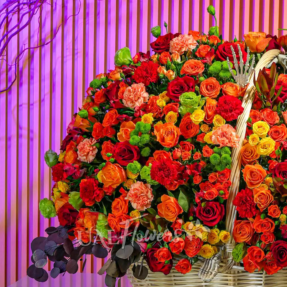Round basket with orange and yellow spray roses, red roses, carnations, chrysanthemums, and Alstroemeria arranged with ribbons