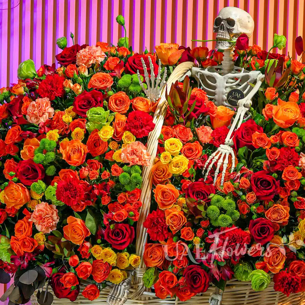 Round basket with orange and yellow spray roses, red roses, carnations, chrysanthemums, and Alstroemeria arranged with ribbons